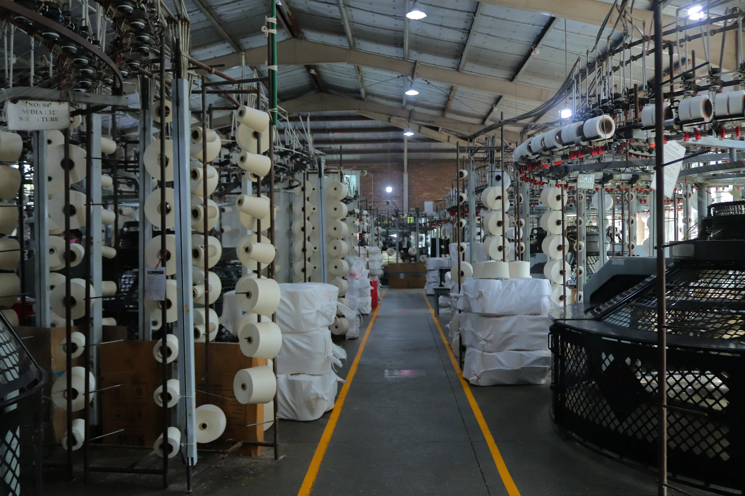 Circular knitting machines and yarn creels lining an aisle on the knitting floor
